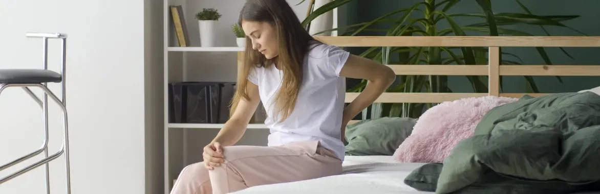 woman seemingly in pain sitting on a bed holding her back